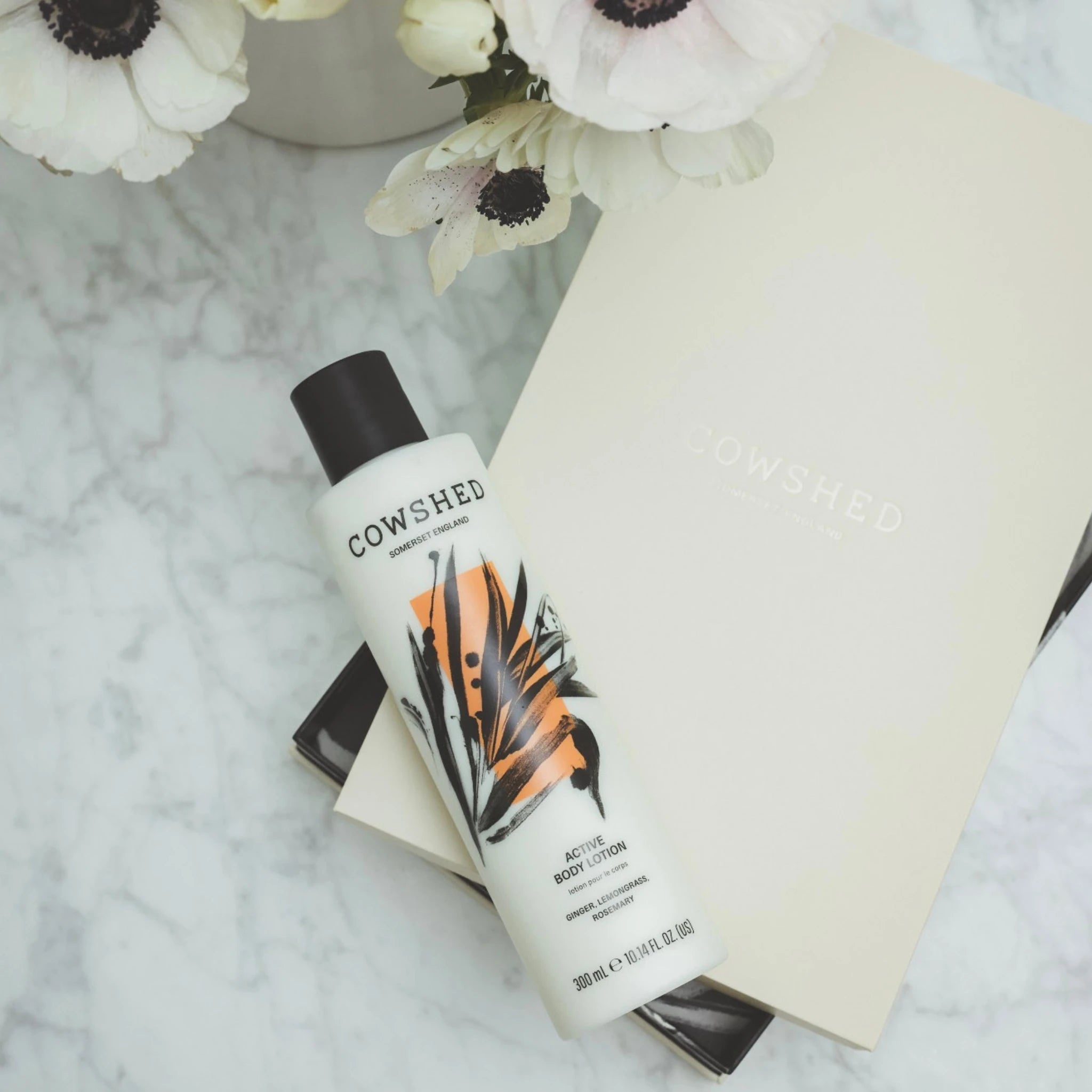 Cowshed Active body lotion bottle on a marble surface with flowers in the background