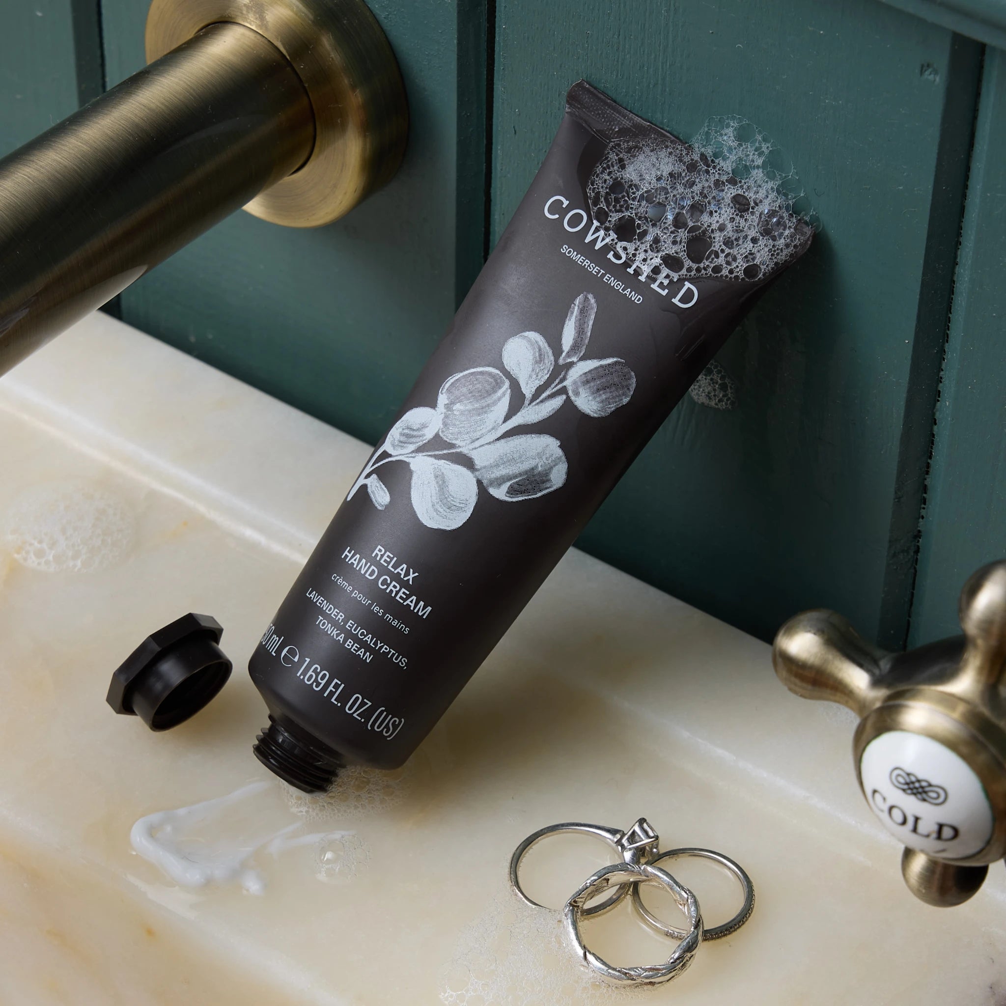 Cowshed hand cream on a bathroom sink with gold faucet and rings.