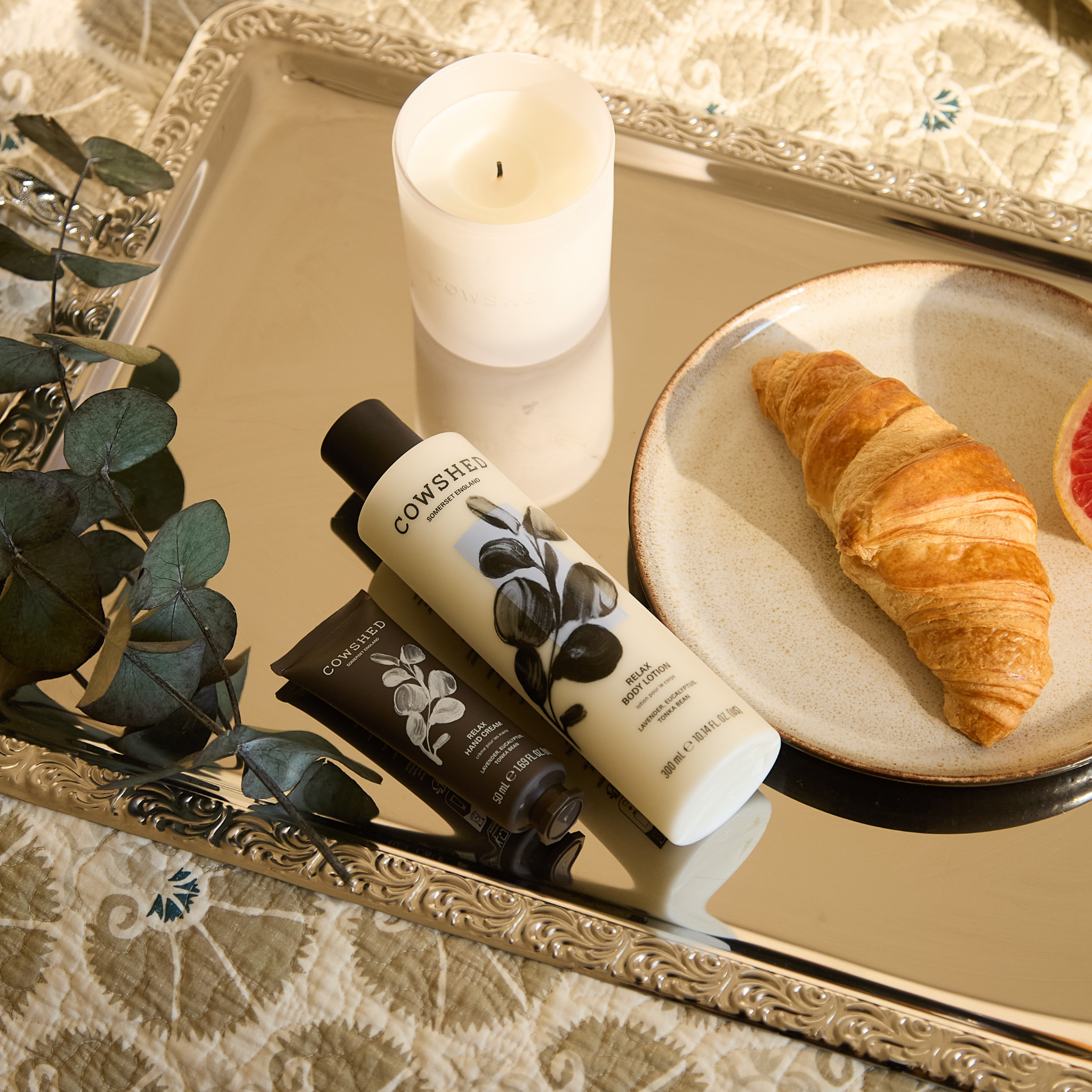 Cosmetic products on a decorative tray with a candle and croissant.