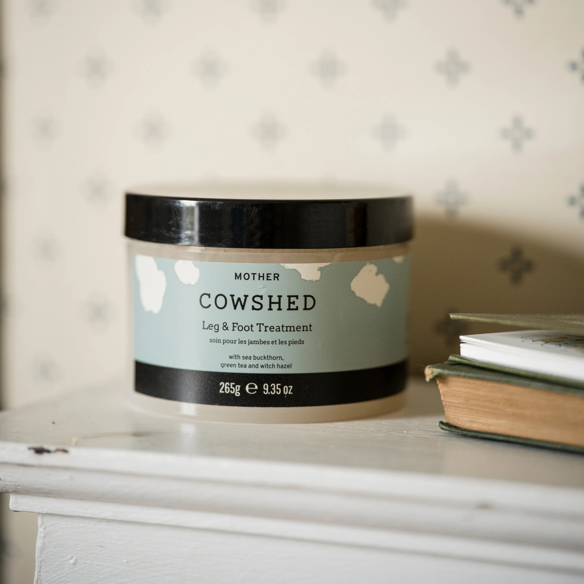 Cowshed leg and foot treatment jar on a surface with a patterned wall in the background