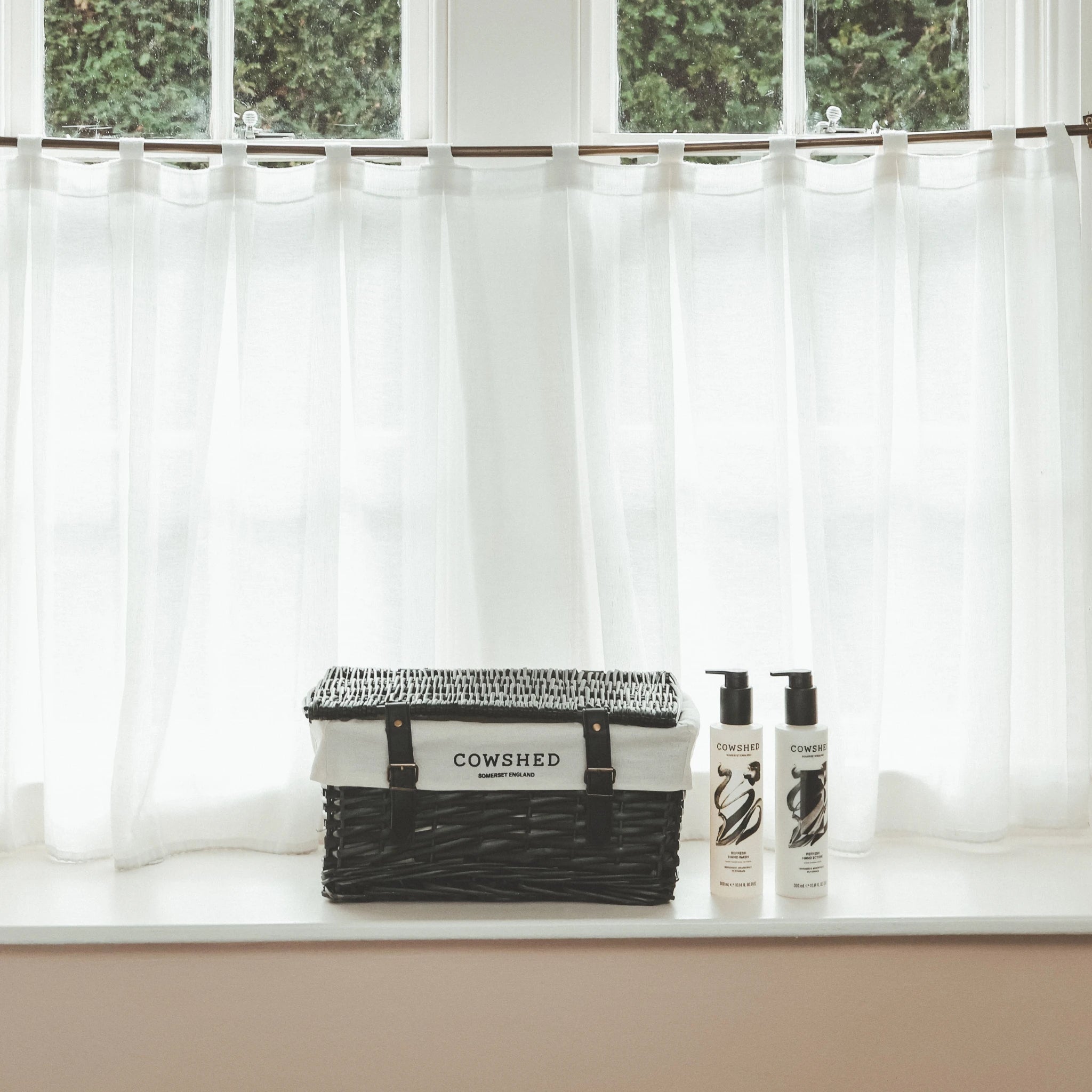 Cowshed products on a windowsill with white curtains