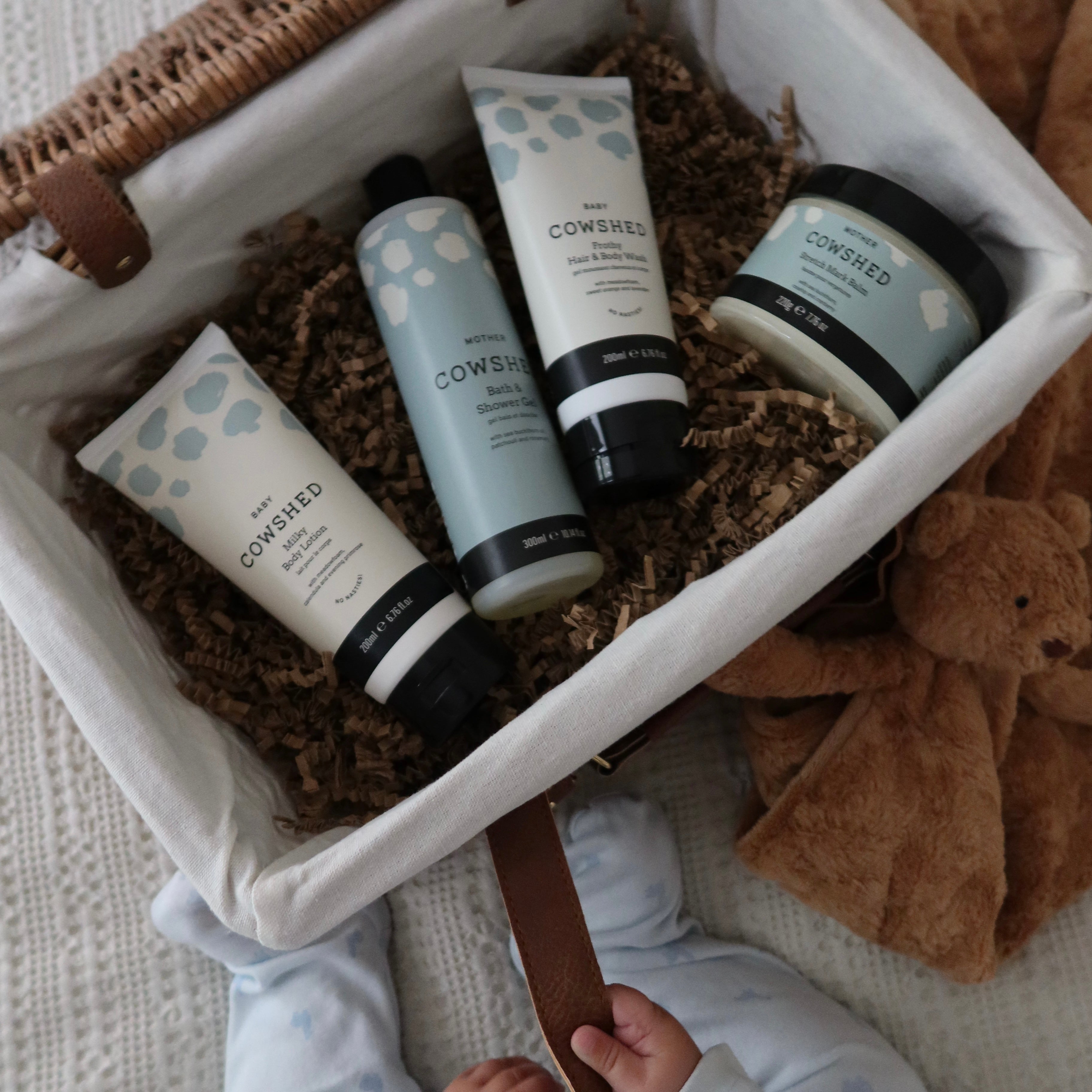 Cowshed baby products in a basket with a teddy bear and child's legs visible