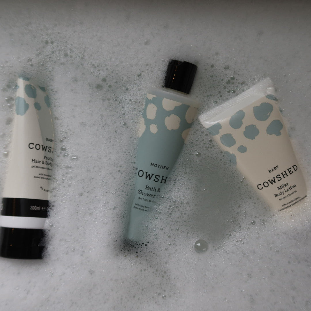 Three Cowshed baby products on a textured gray surface