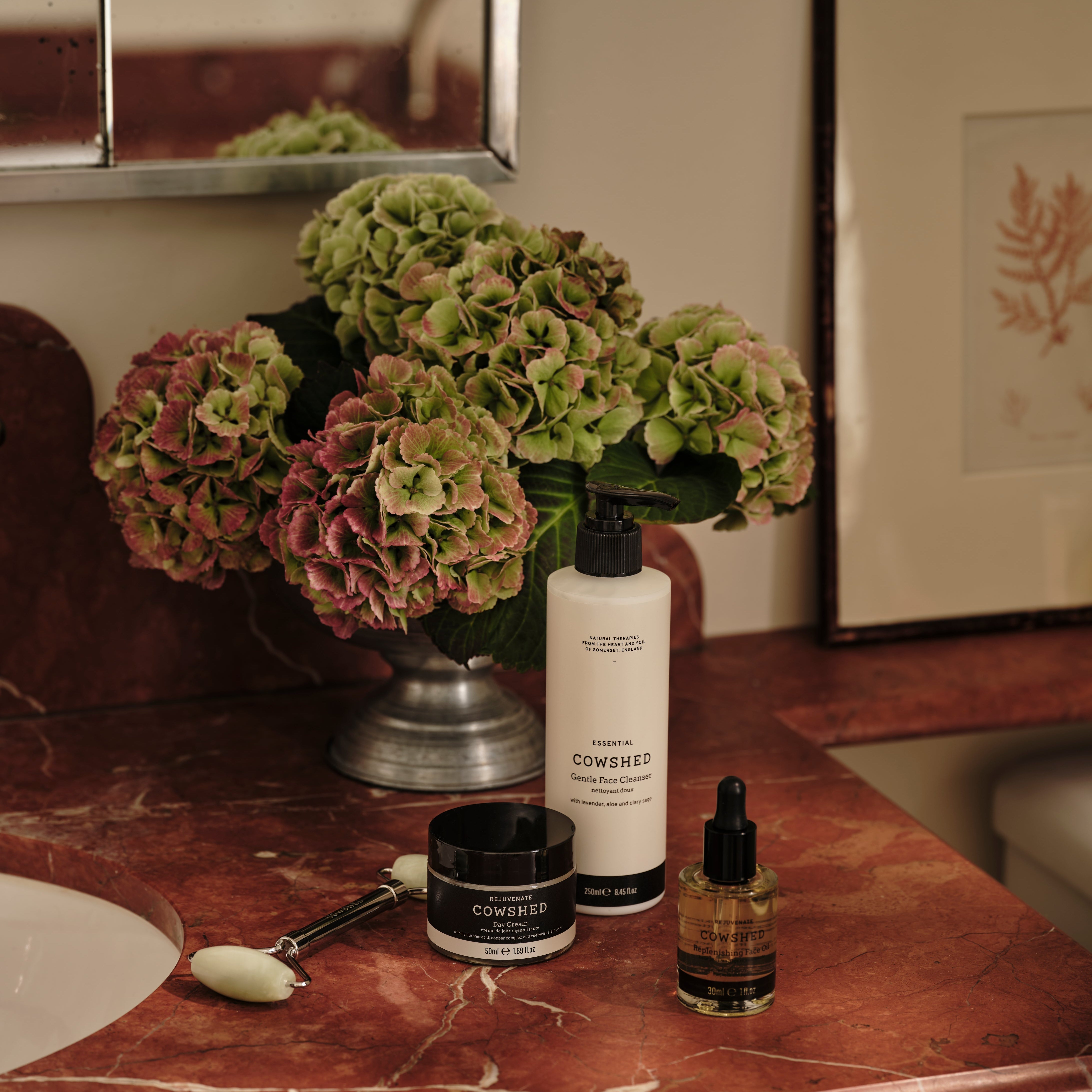 Cosmetic products on a marble counter with flowers and a mirror in the background