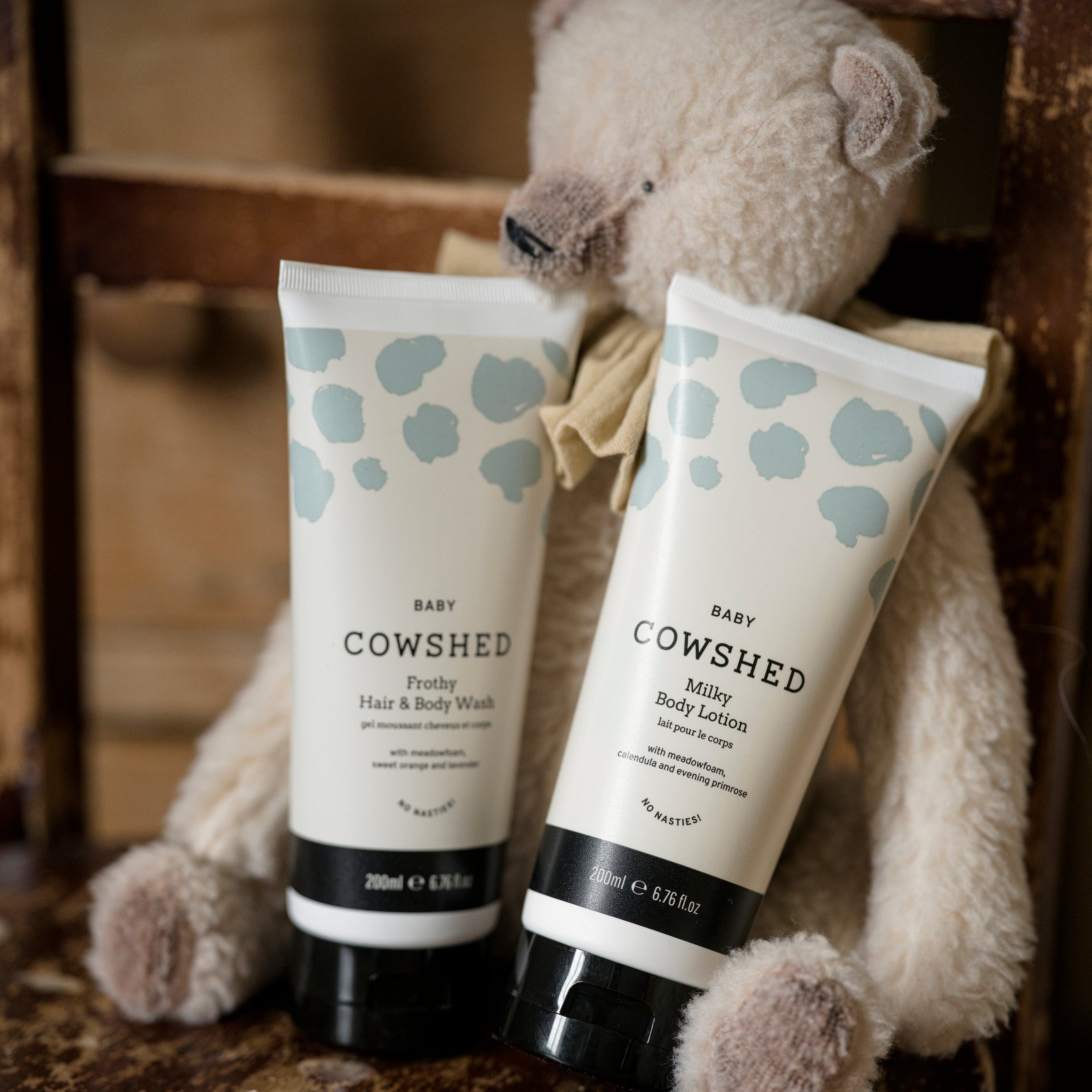 Two Cowshed baby products next to a teddy bear on a wooden surface