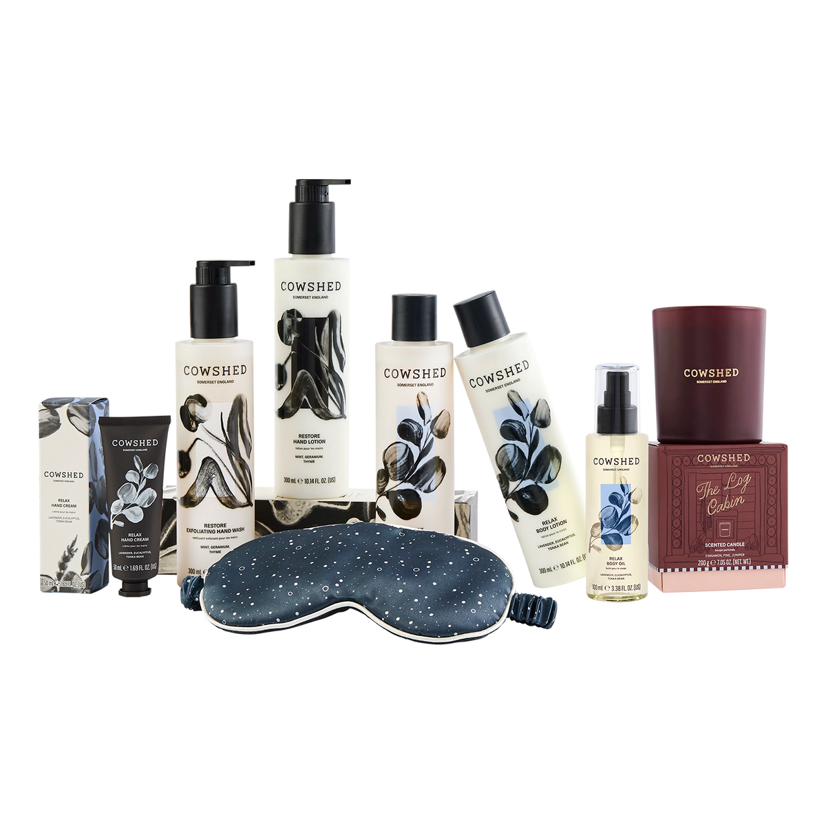 Cowshed Self Care Gift Set featuring hair and body care products including shampoo, conditioner, body wash, and lotion, alongside a starry blue sleep mask and a candle on a white background.