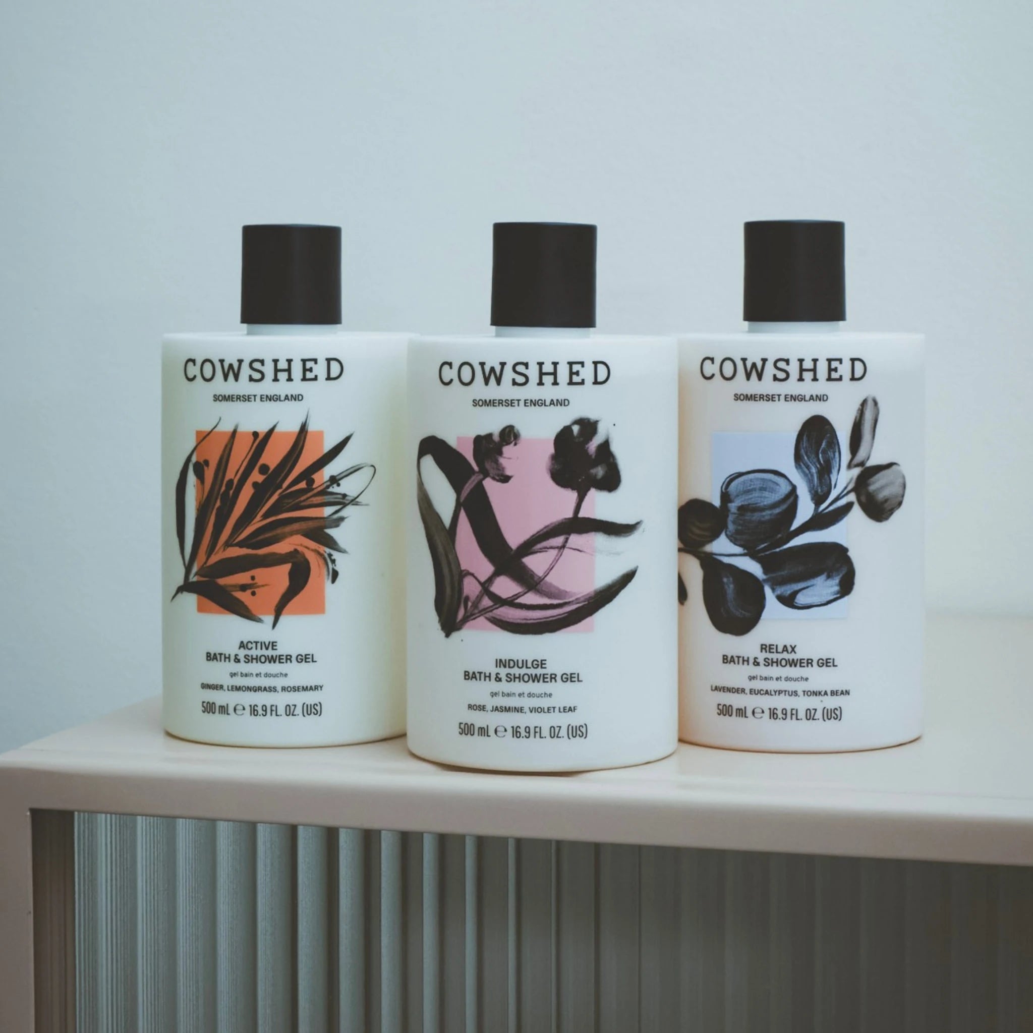 Three Cowshed bath and shower gel bottles on a shelf with a light gray background