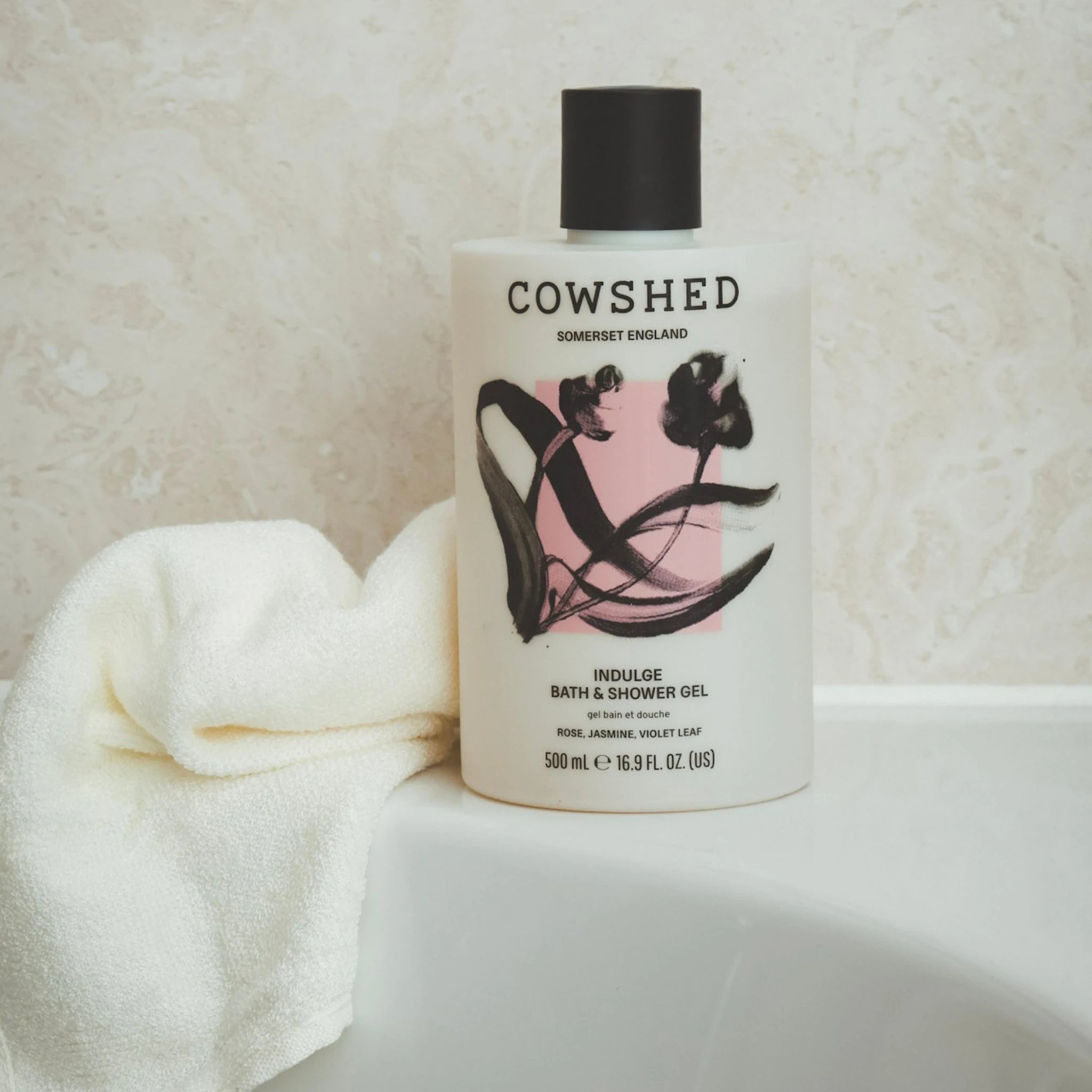 Cowshed Indulge bath and shower gel bottle with a towel on a neutral background