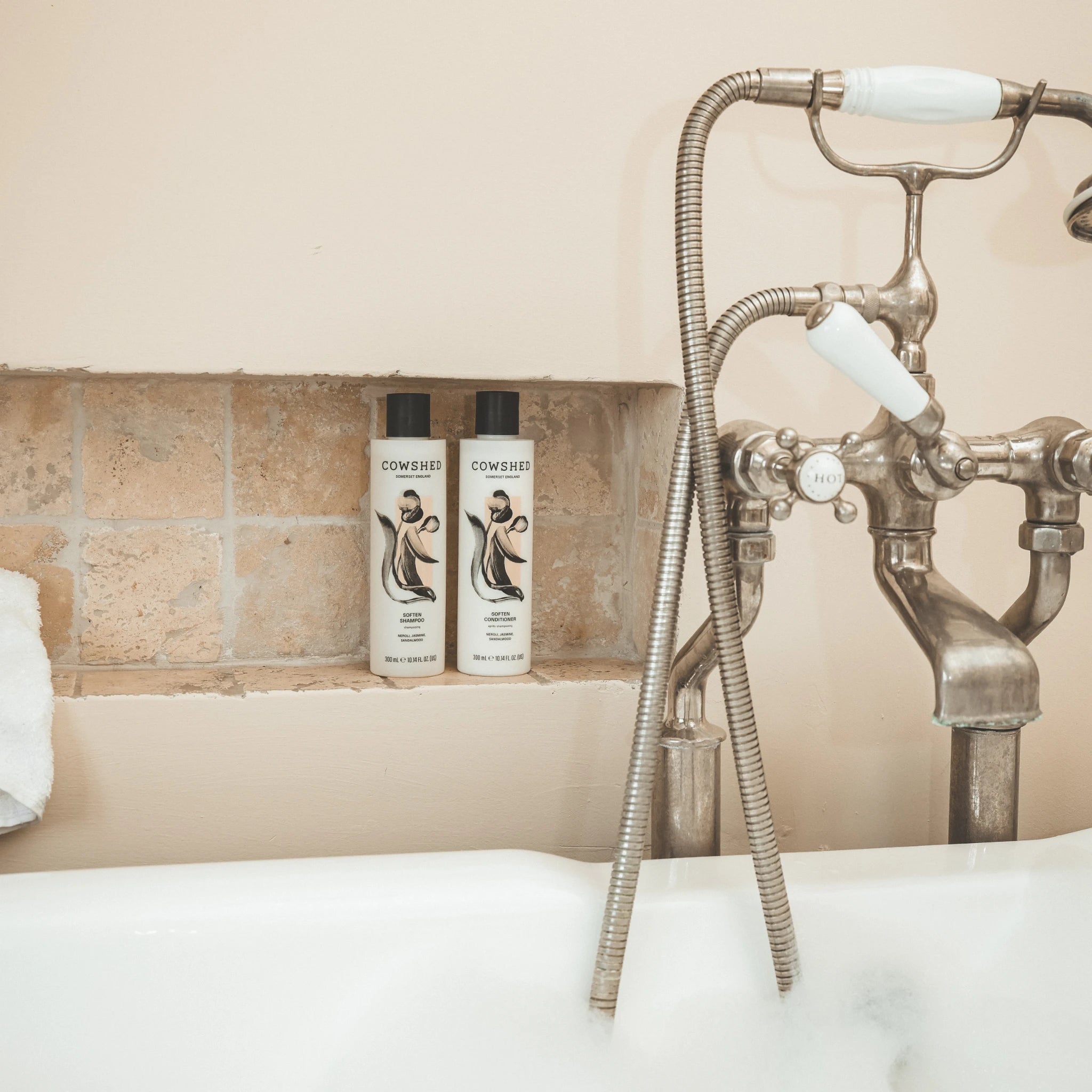 Cowshed Soften Shampoo & Conditioner on a bathroom shelf with a vintage-style shower head