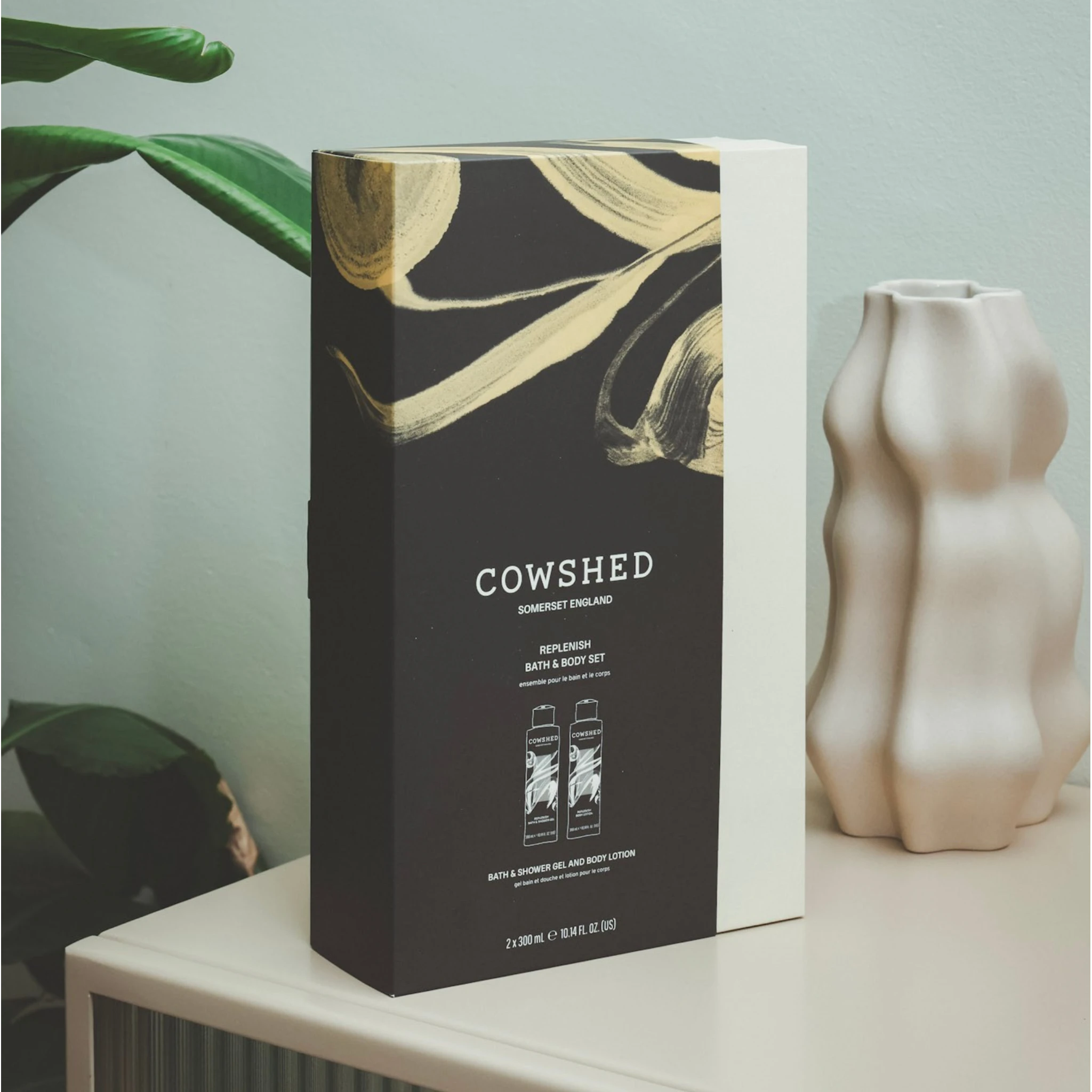 Cowshed product packaging on a table with a plant and vase in the background