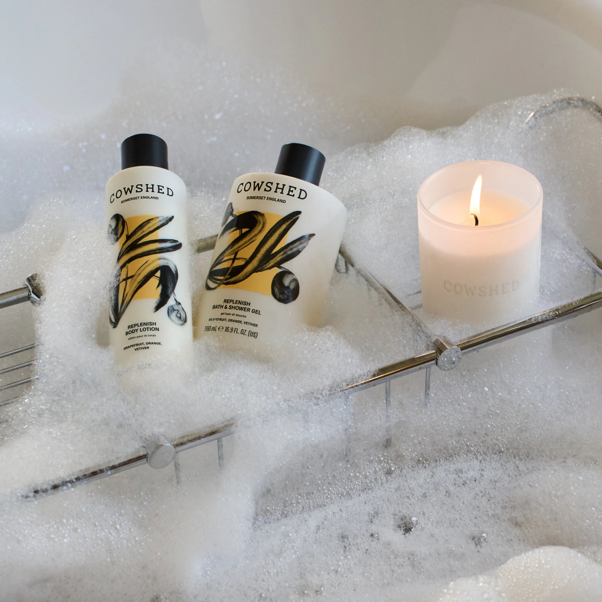 Two Cowshed bottles in a bubble bath with a lit candle.