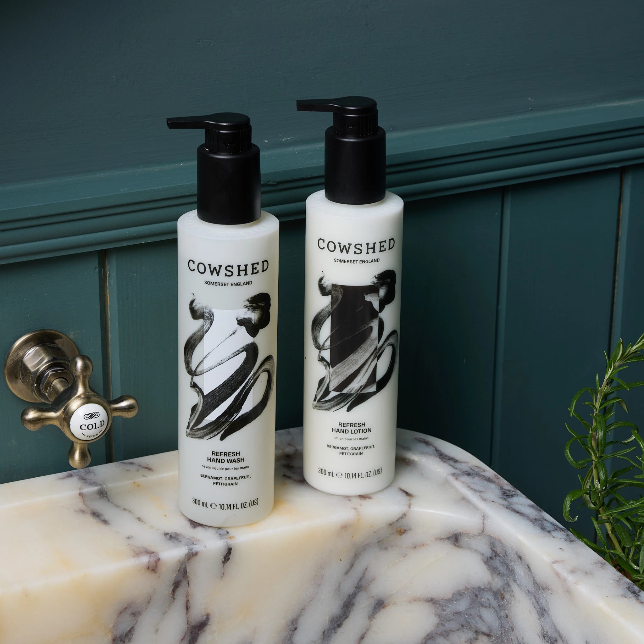 Two Cowshed hand wash products on a marble sink with a green wall in the background.