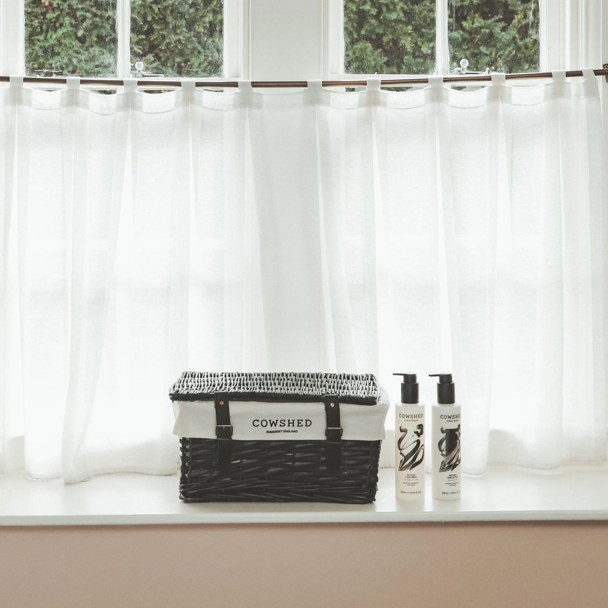 Cowshed products on a windowsill with white curtains