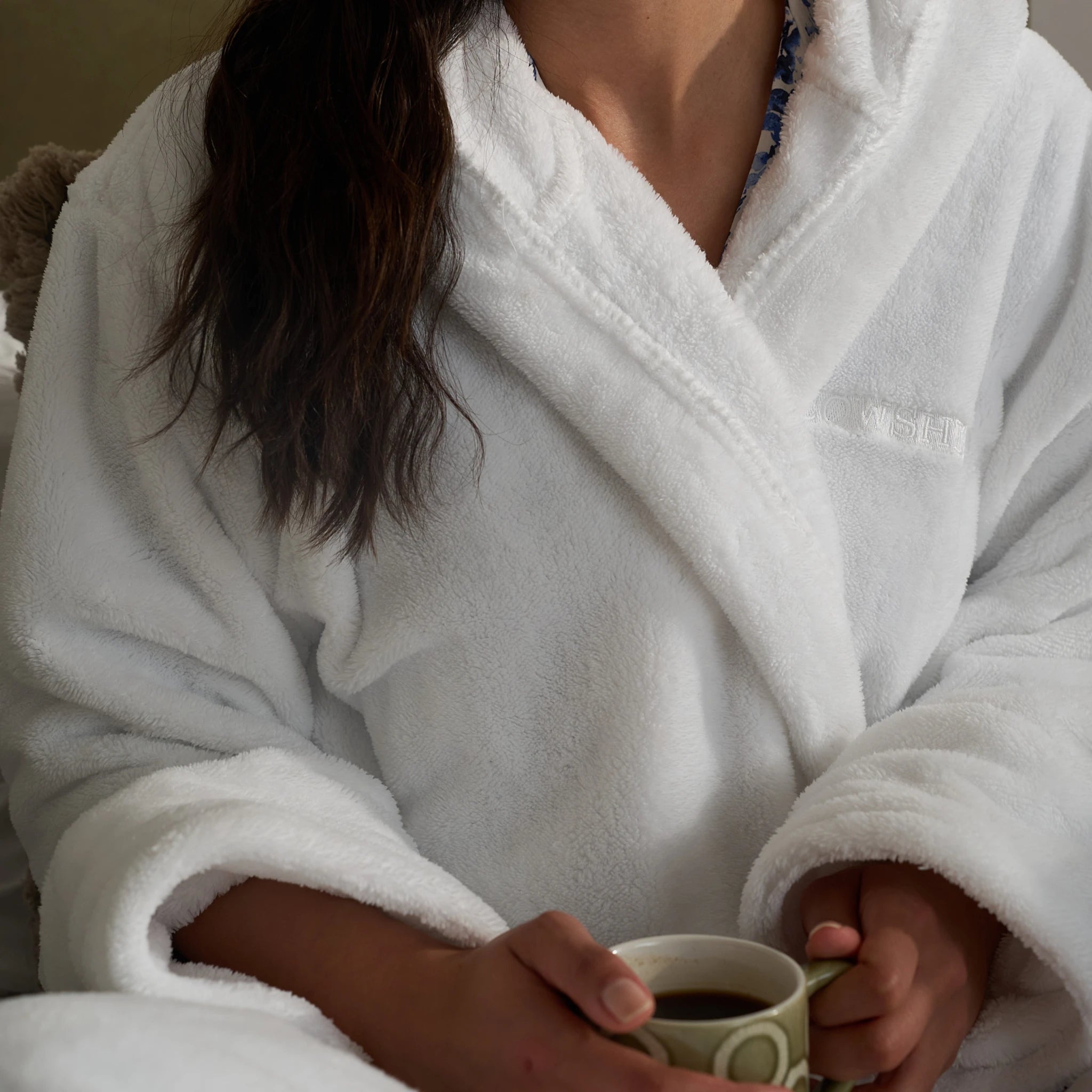 Person wearing a white robe holding a mug with a blurred background