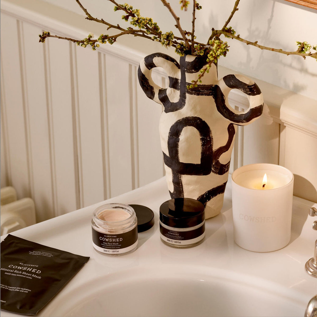 Cowshed skin care range on white sink with a lit cowshed candle