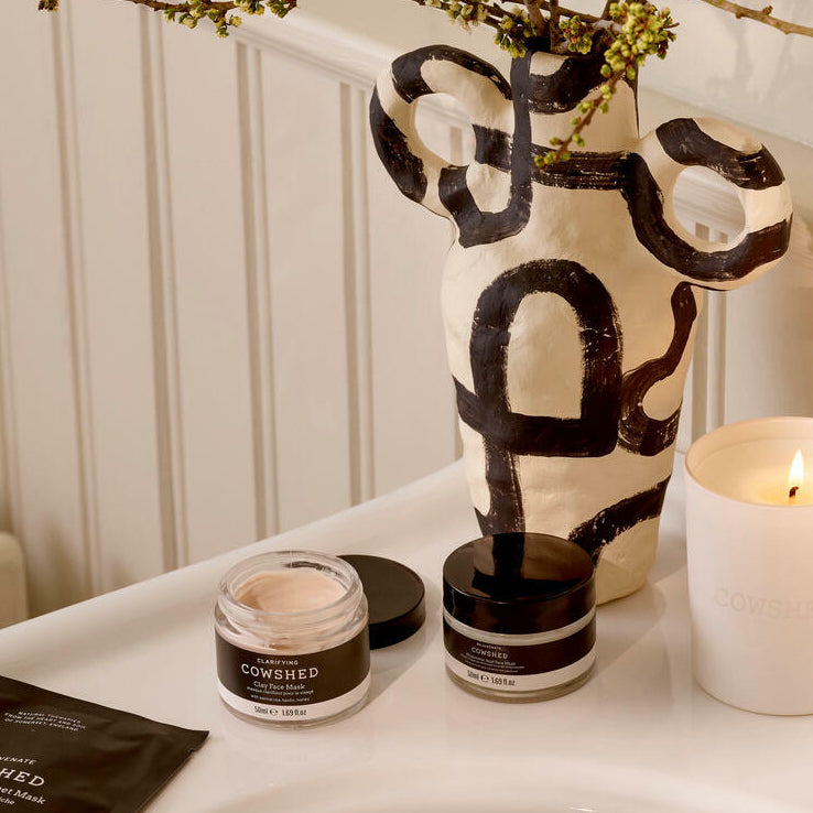 Cowshed skincare products on a table with a decorative vase and candle.