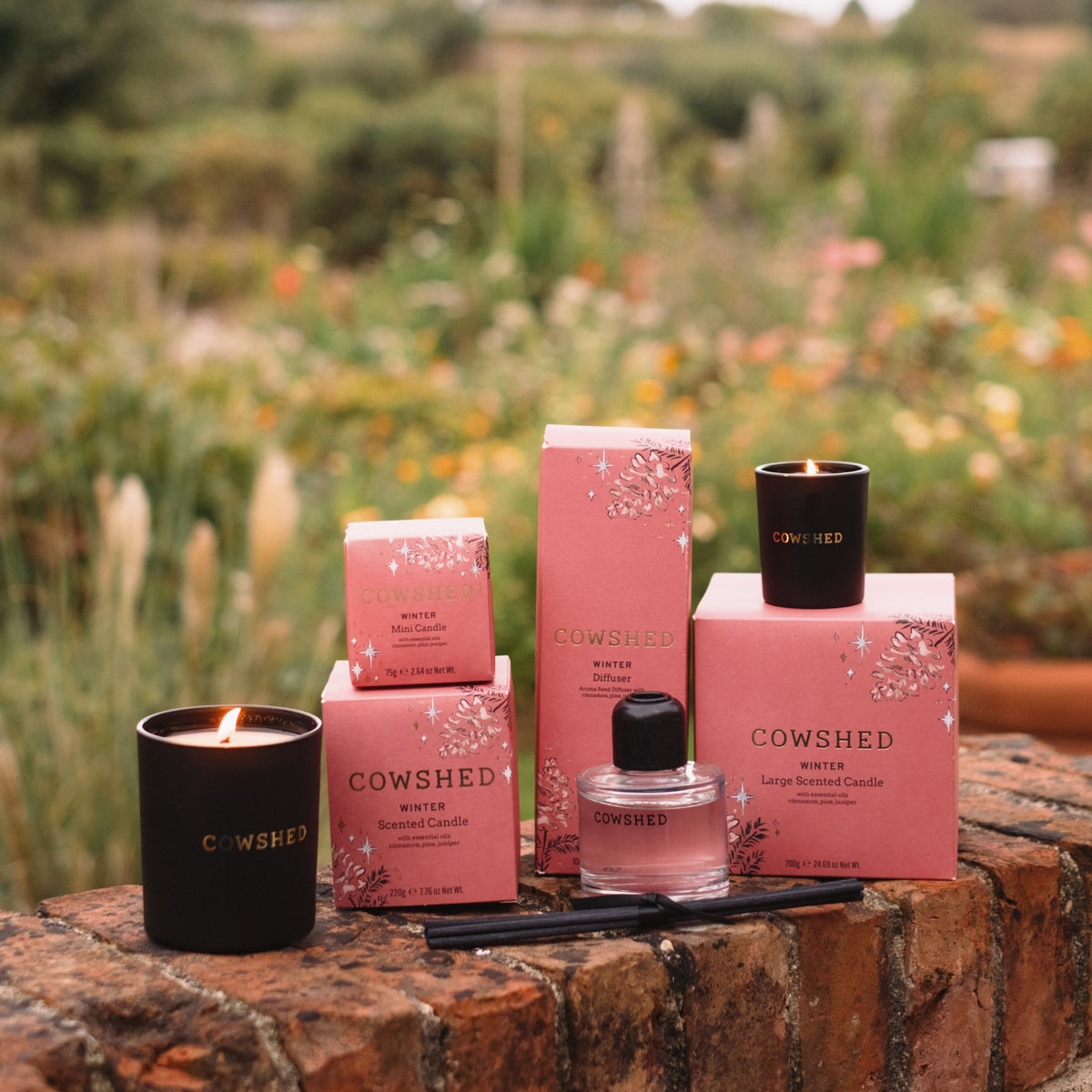 Cowshed products including candles and bottles on a brick ledge with a garden background