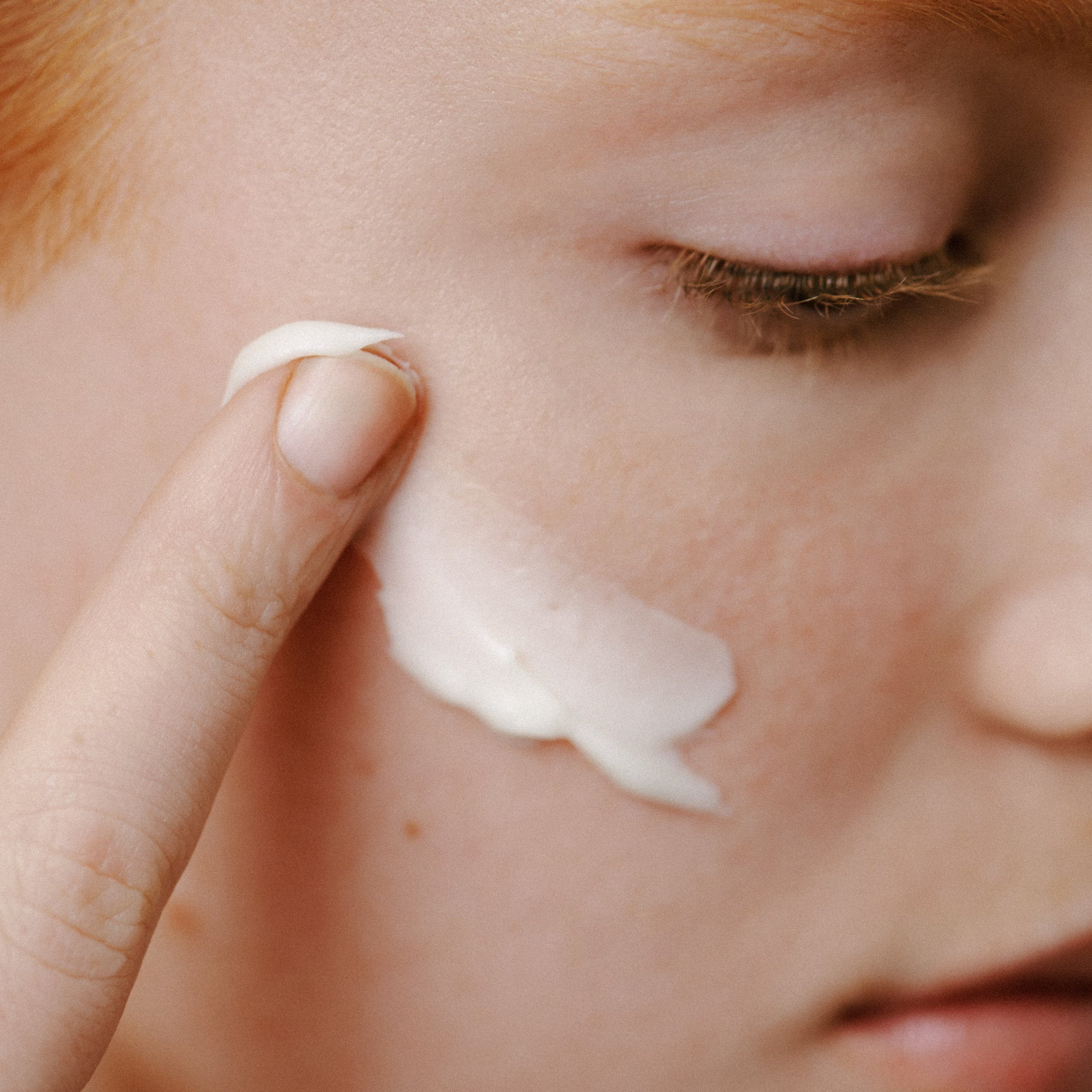 Close-up of a person applying cream to their face with a finger.