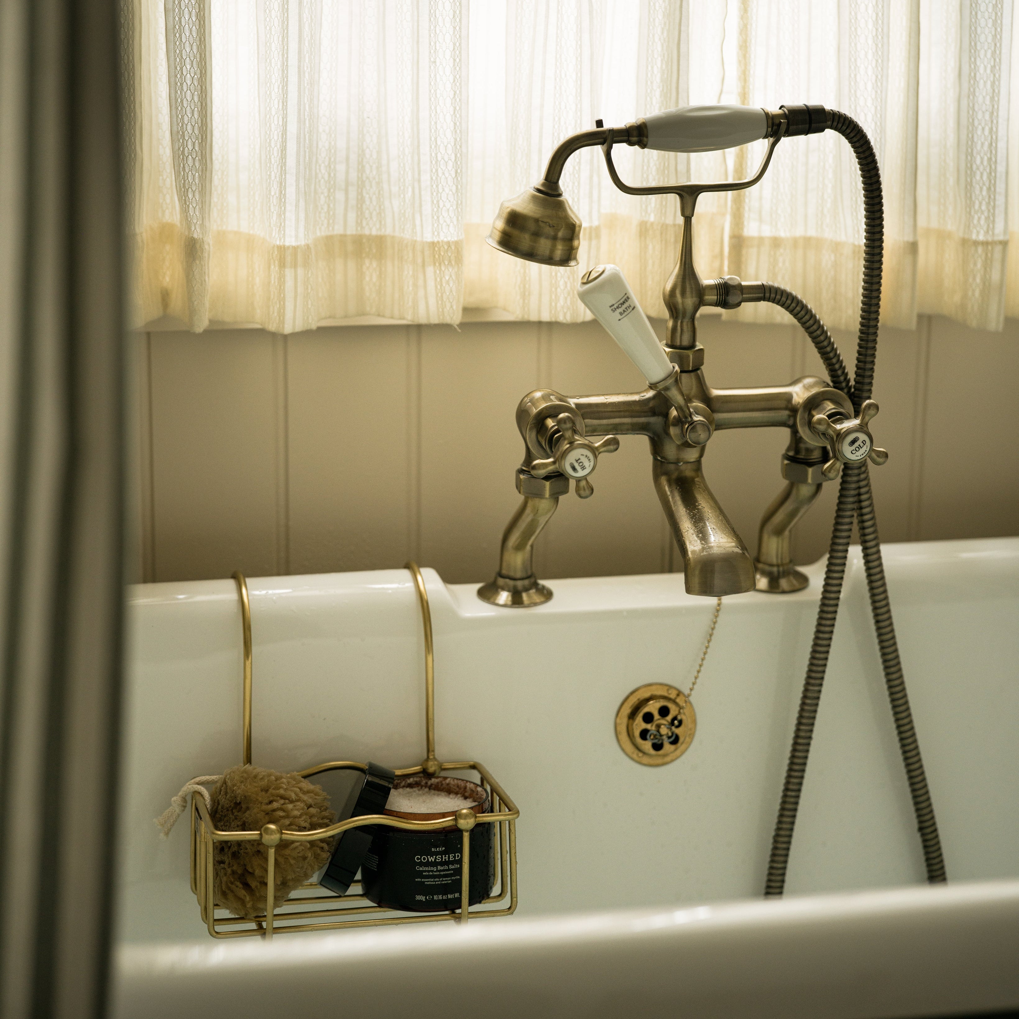 Vintage-style bathtub with brass faucet and shower head, surrounded by white curtains.